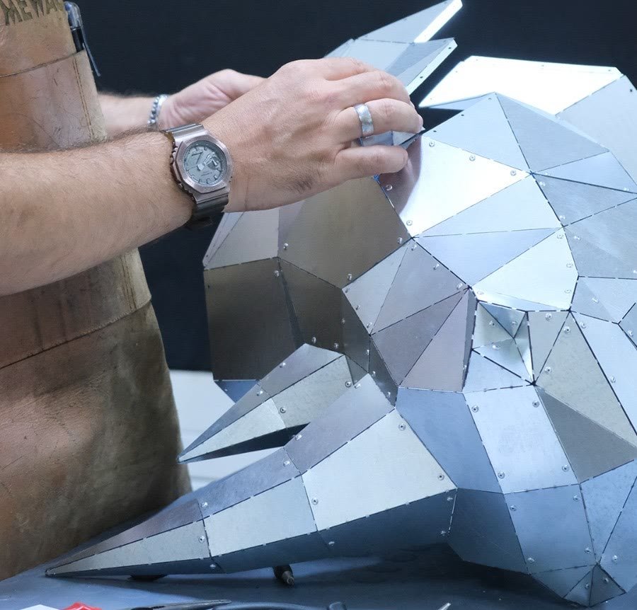 Un artesano de MewaCraft monta a mano en el taller una cabeza escultórica low-poly con piezas de acero galvanizado