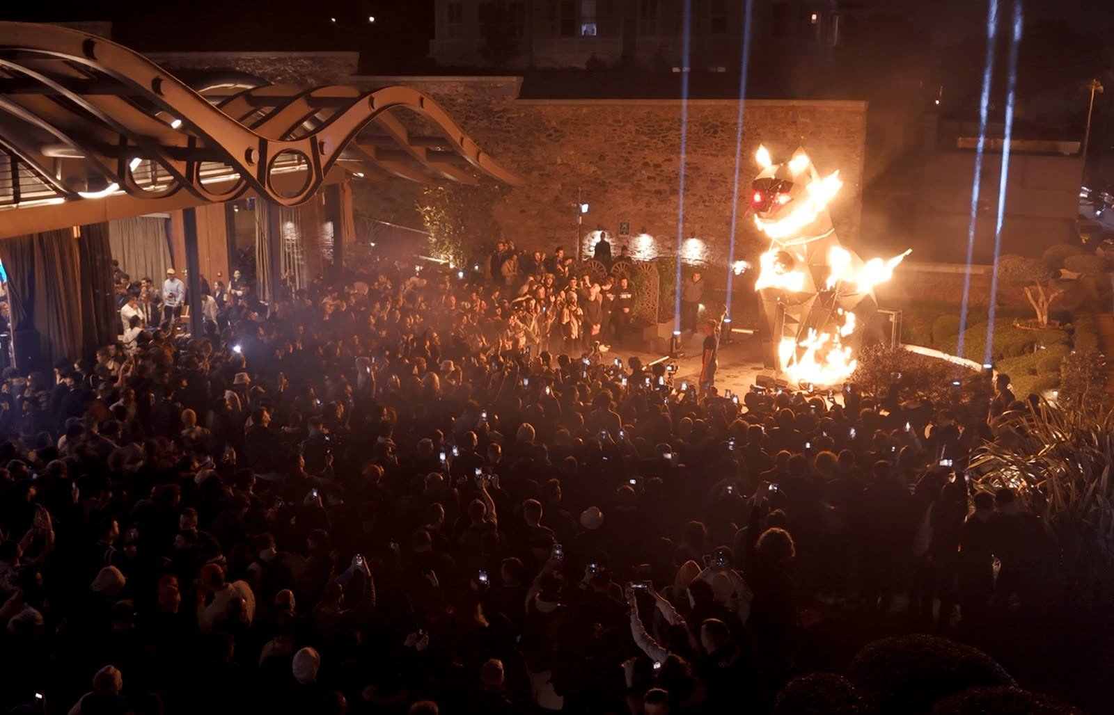 The monumental metal cat sculpture with flame effects at a night launch, surrounded by the audience
